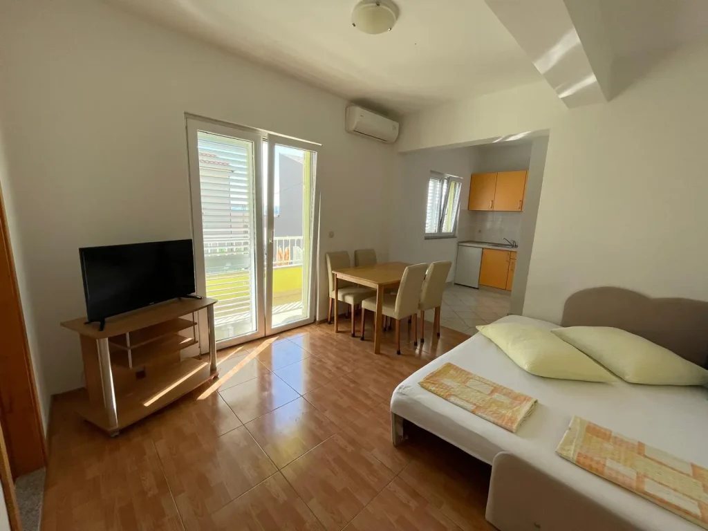 Dnevna soba apartmana 1 s kaučem, stolom, potpuno opremljenom kuhinjom i prozorima koji vode na sunčani balkon.